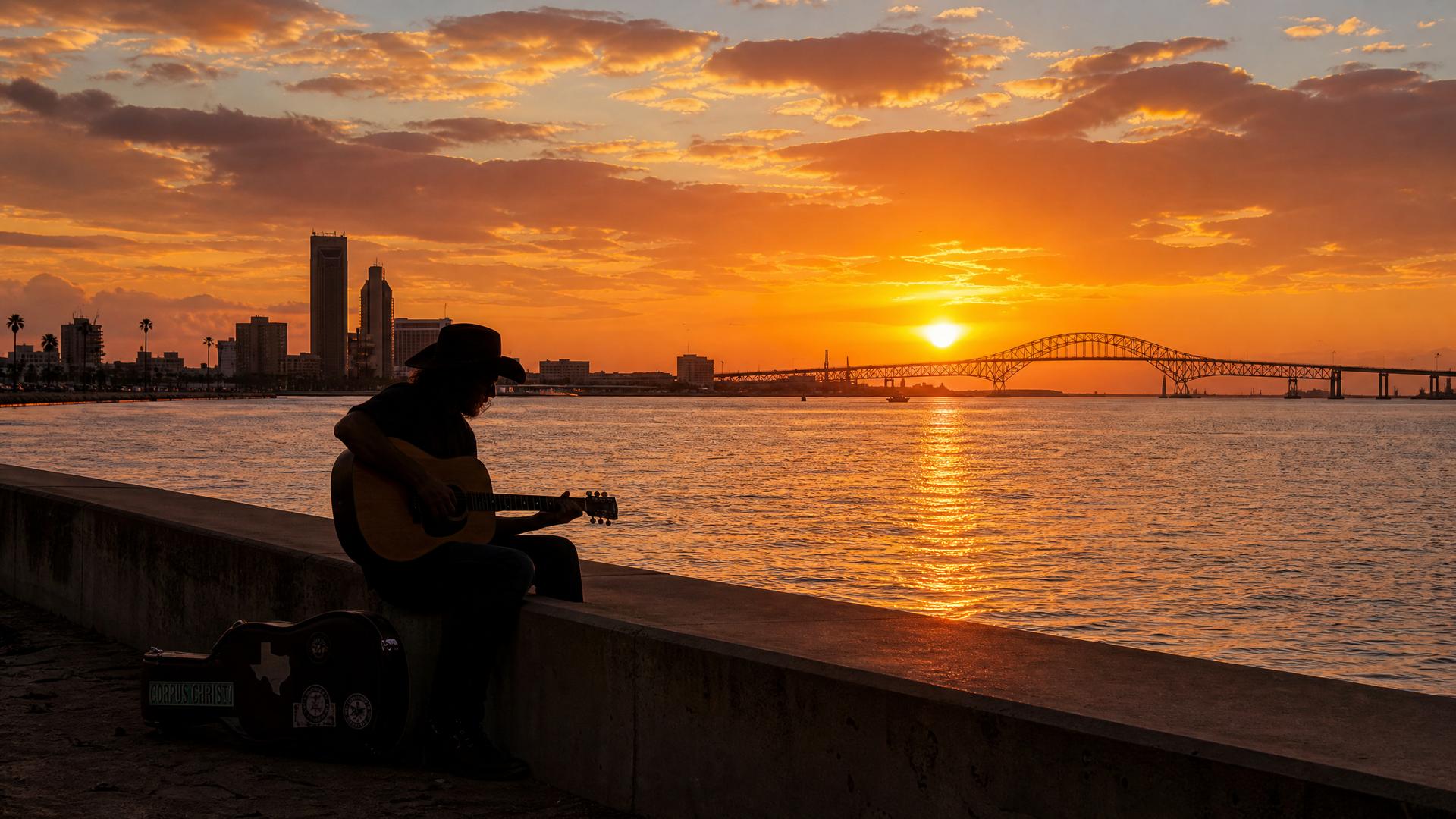 A musician silhouetted against a golden sunset over Corpus Christi Bay
